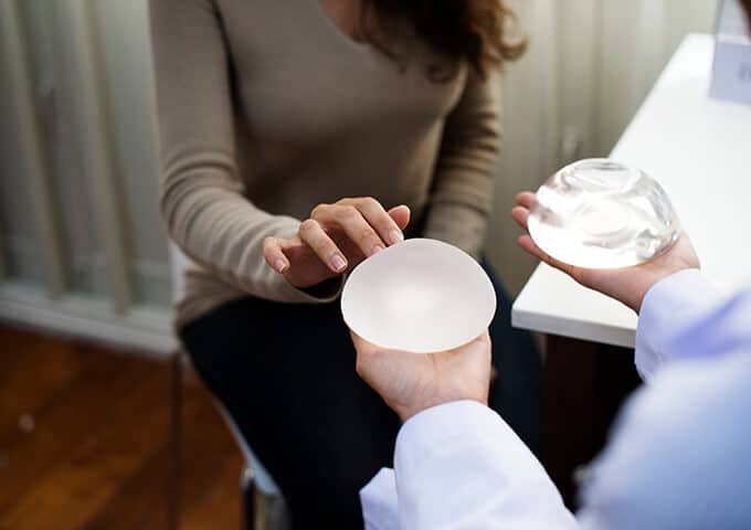 Doctor holding breast implants and a woman touching them