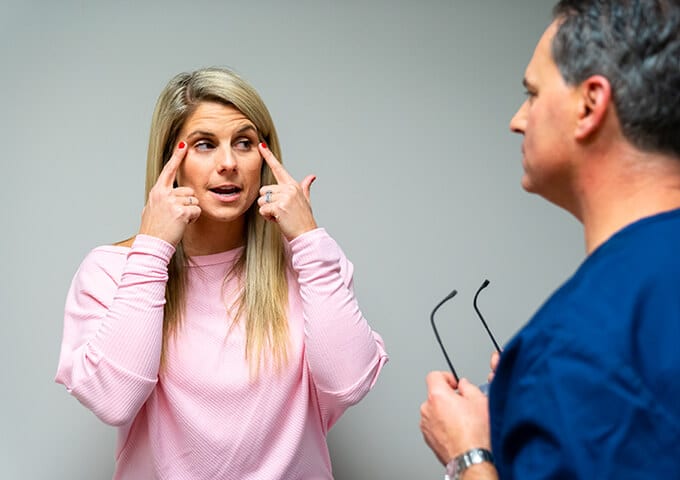 Woman pointing to her eyes in front of a surgeon